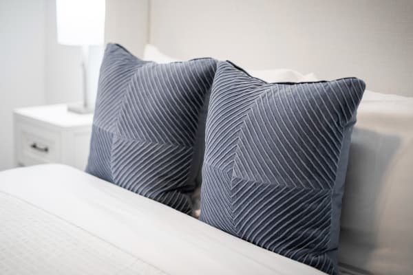 Two navy blue decorative pillows with striped patterns on a white bed.