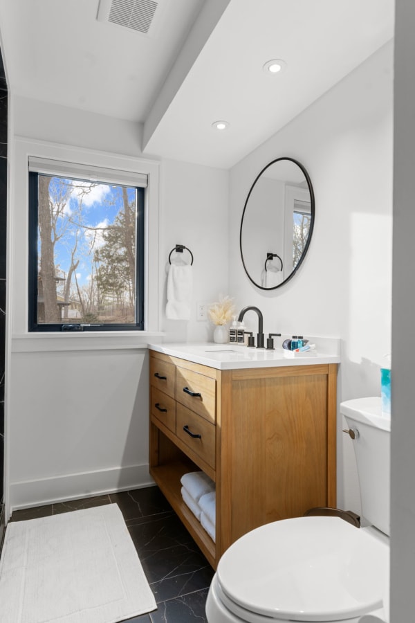 Modern bathroom featuring a wooden vanity, round mirror, and natural light.