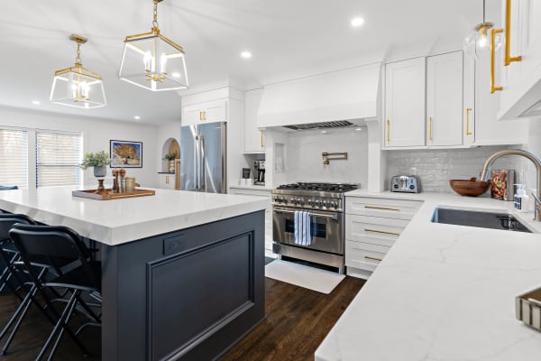 A modern kitchen with a marble island, white cabinetry, and gold fixtures.
