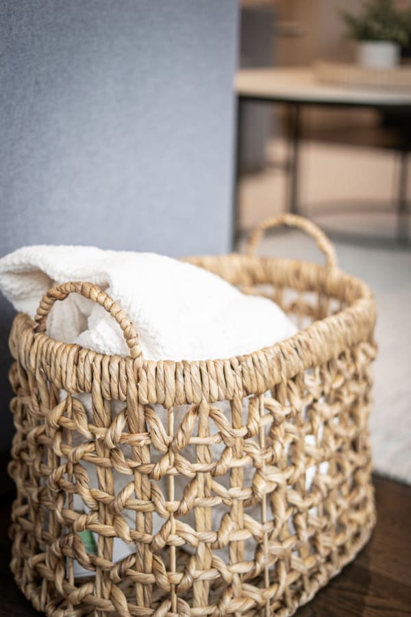 A woven basket holding a white blanket against a grey background in a modern room.