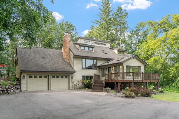 Two-story house with a wooden deck and a garage in a wooded area.