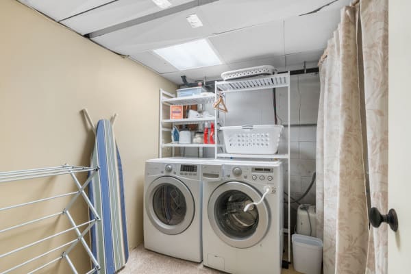 A modern laundry room featuring stacked washing machines, a striped ironing board, and organized storage.