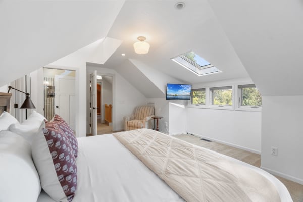 Cozy attic bedroom with white walls, a skylight, and a striped armchair.