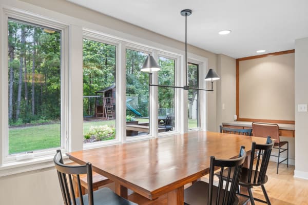 Bright dining area featuring a wooden table, black chairs, and large windows with garden view.