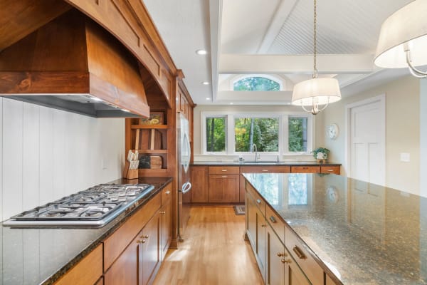 Interior view of a stylish kitchen with dark granite countertops and wooden cabinets, featuring large windows and modern lighting.