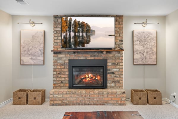 A cozy living room with a brick fireplace and a modern TV showcasing a tranquil landscape.