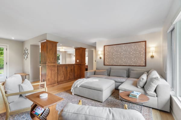A modern living room with a large gray sectional couch, wooden coffee table, and bright windows.