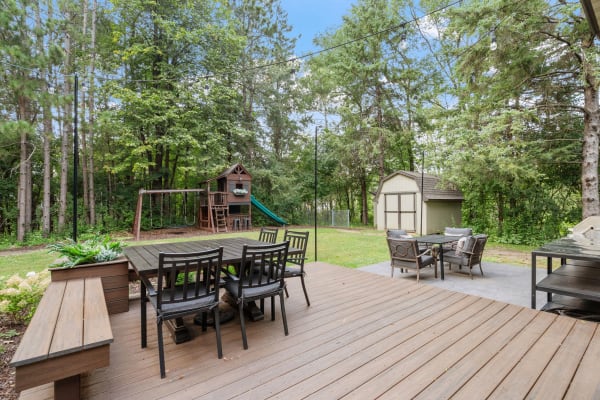 An outdoor wooden deck featuring a dining area and a playground, with trees in the background.