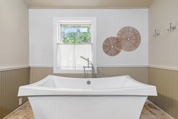 A bright bathroom with a white bathtub and a window, adorned with woven wall decor.