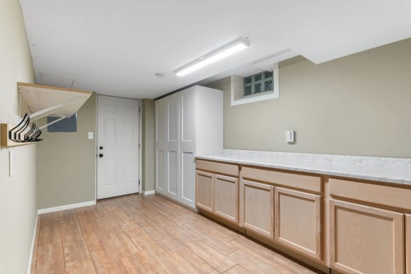 A bright laundry room featuring a coat rack, double doors, and wooden cabinets with marble counters.
