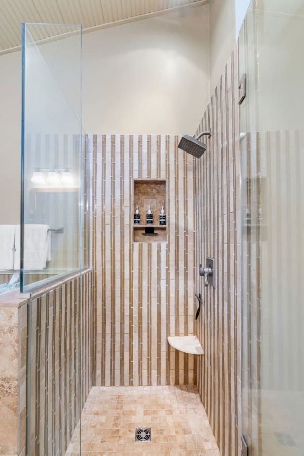 Modern shower with glass walls and beige stone tiles, featuring a built-in niche for shower products.