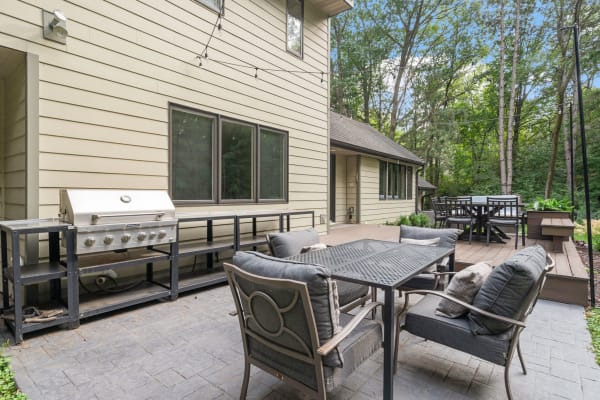 Outdoor patio featuring a grill, cushioned seating, and a dining table amidst greenery.