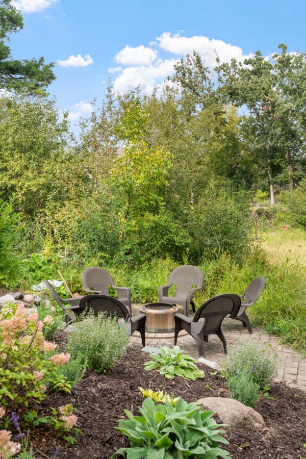 Outdoor seating with wicker chairs and a fire pit in a green garden setting.