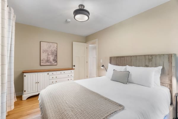 Cozy bedroom featuring a bed with white linens, a wooden dresser, and warm lighting.