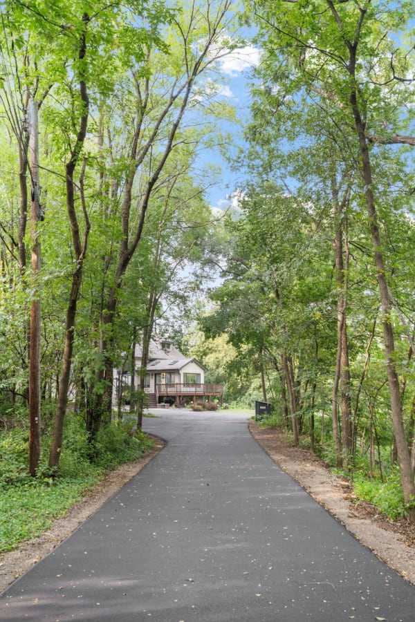 A paved road surrounded by lush trees that leads to a house.