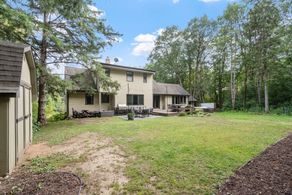 Two-story house with outdoor seating and grill in a green landscape.
