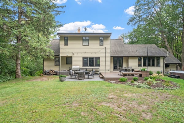 A two-story beige house with a backyard deck and green lawn.