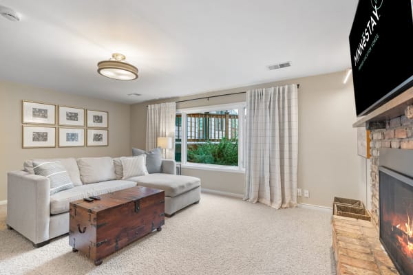 A well-decorated living room featuring a light gray sectional sofa, wooden trunk, and a fireplace.