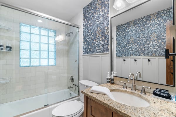 Modern bathroom with glass block window and floral wallpaper.