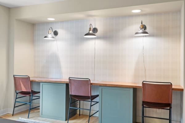 A contemporary workspace featuring a wooden desk with three metal lamps and leather stools.