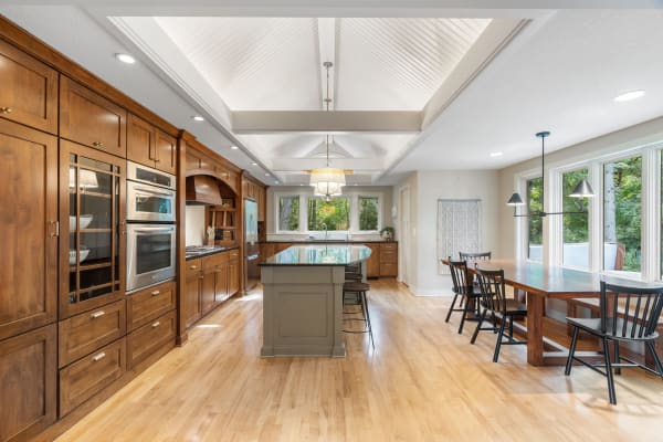 Spacious kitchen with wooden cabinetry, dark granite island, and a dining area by large windows.
