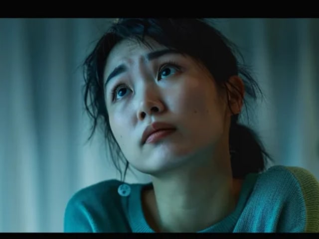 An Asian woman sitting quietly by a lamp, looking up in thought