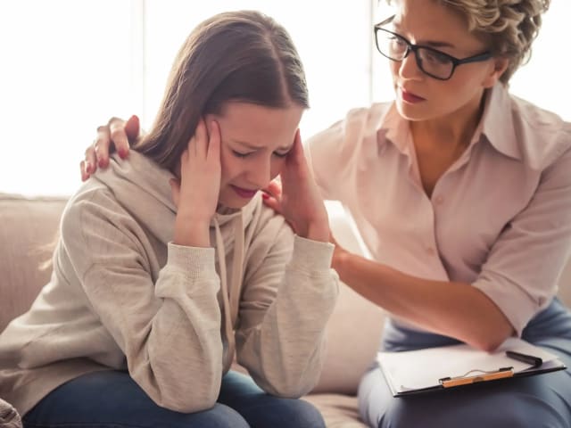 A teen on a couch with a counselor offering support