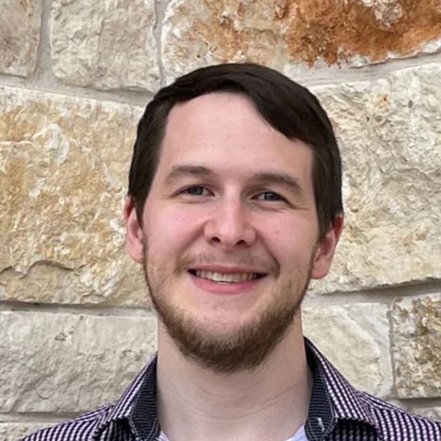 Oliver Papa-Garcia smiling in front of a stone wall