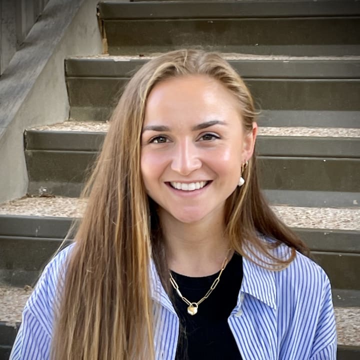Bailey Pellissier smiling on grey steps in a striped shirt