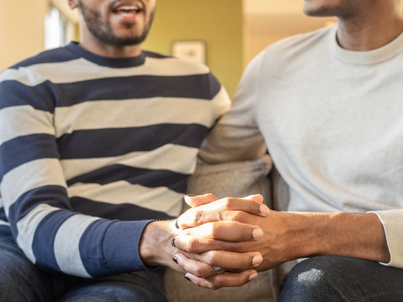 Two people sitting together on a couch, hands clasped