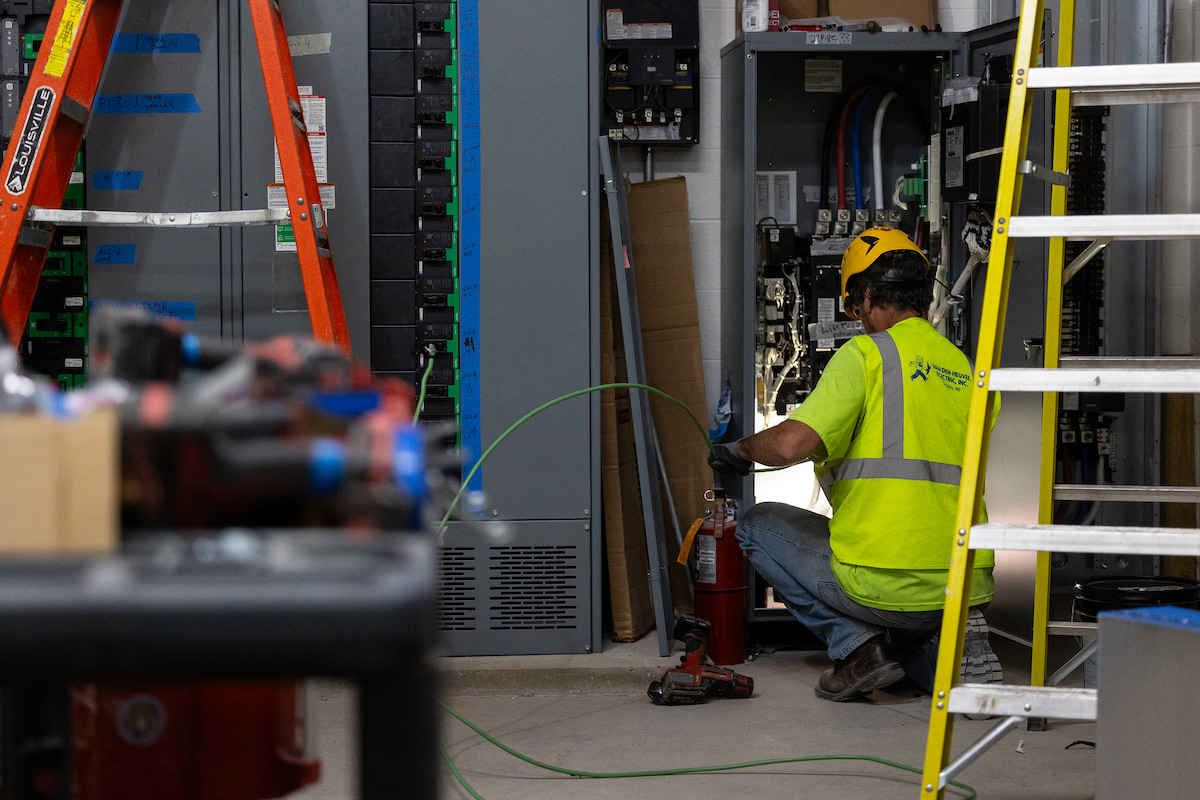 Man in yellow shirt kneeling on the floor working with electrical wires