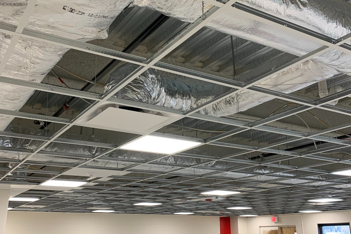 Commercial HVAC ductwork installation above a drop ceiling with reflective insulation and lighting