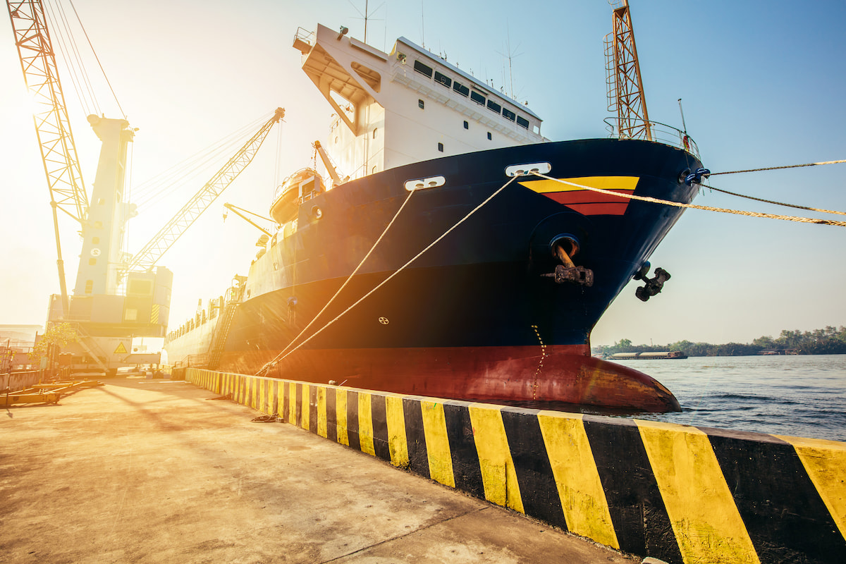 Large ship docked at a pier and being loaded by a crane