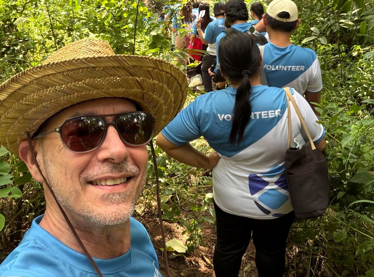 Andy Schachtel in a straw hat and sunglasses taking a selfie with Sourcefit volunteers on a forest trail