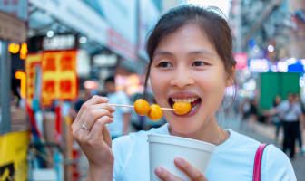 Jeune femme asiatique mangeant des fish balls dans les rues de Hong Kong