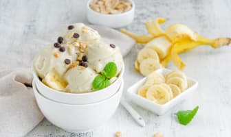 Glace à la banane vegan faite maison dans un bol avec cacahuètes et chocolat