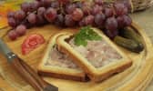 2 tranches de pâté en croûte posées sur un plateau en bois, avec couteau, raisins, tomate et cornichons