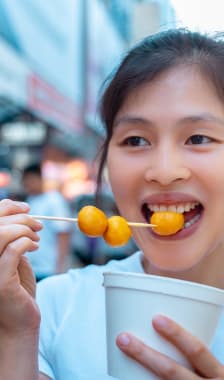 Jeune femme asiatique mangeant des fish balls dans les rues de Hong Kong