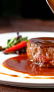 Un filet de bœuf grillé, servi sur une assiette blanche avec une sauce demi-glace