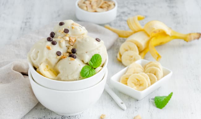 Glace à la banane vegan faite maison dans un bol avec cacahuètes et chocolat