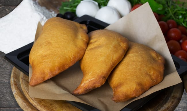 Panzerotti posés sur papier sulfurisé et assiette noire.