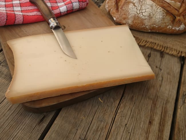 Morceau de beaufort tranché avec couteau, pain et serviette sur une table en bois