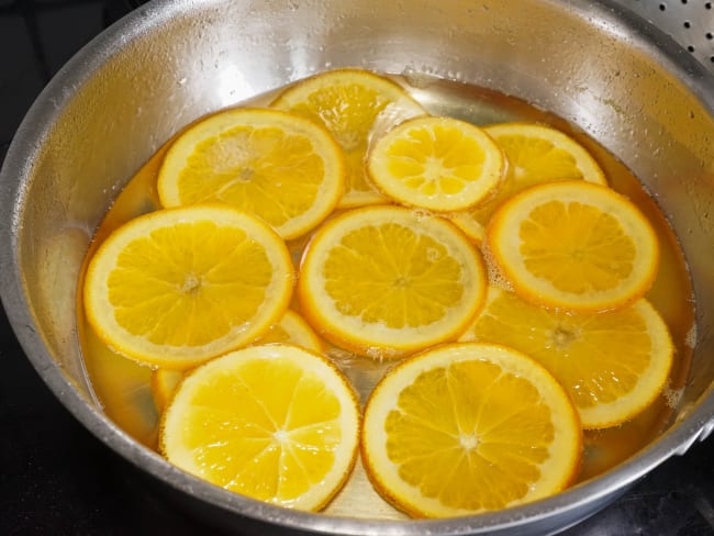 Tranches d'oranges en train de confire dans une casserole.