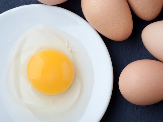 Oeuf entier cru sur assiette blanche