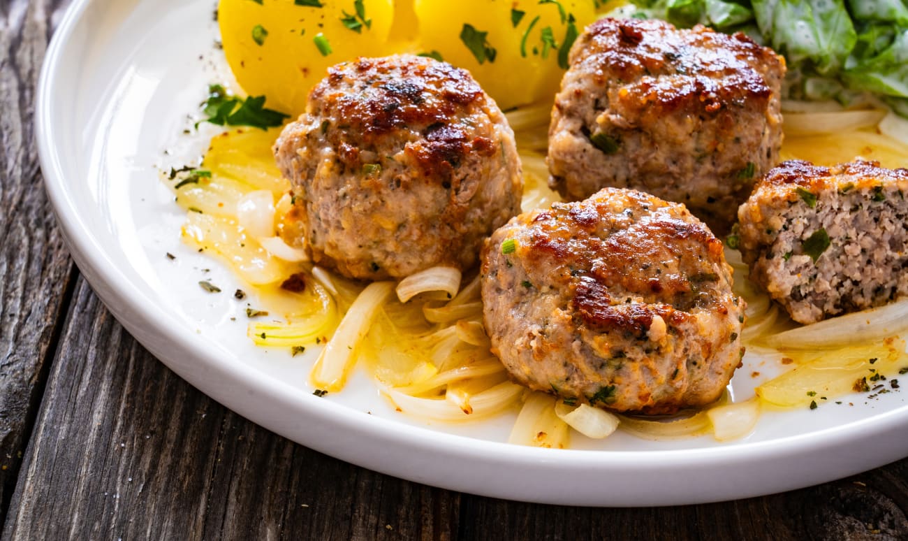 Boulettes de porc poêlées avec oignon frit, pommes de terre bouillies et laitue à la crème sur table en bois