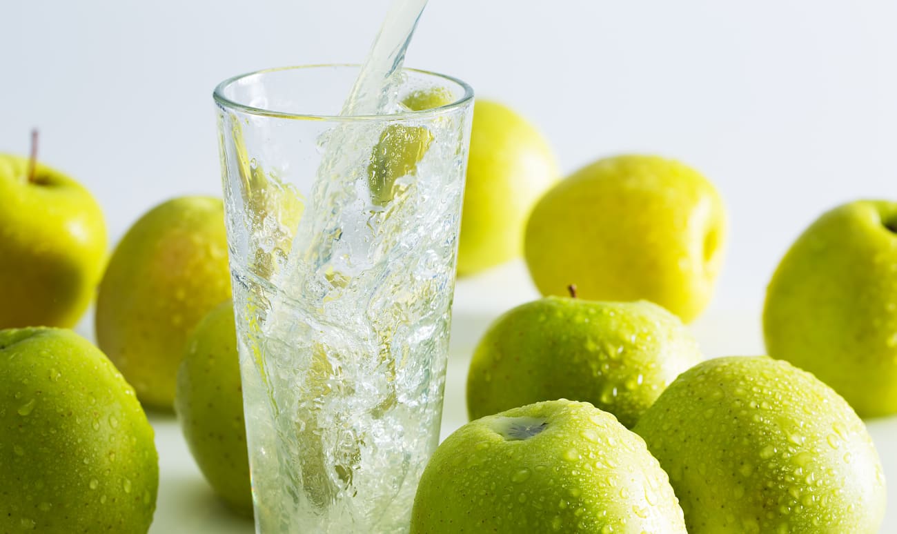 Verre de Manzana sur glace entouré de pommes vertes