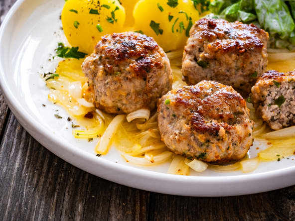 Boulettes de porc poêlées avec oignon frit, pommes de terre bouillies et laitue à la crème sur table en bois