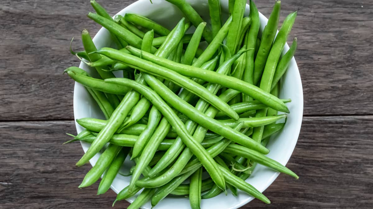 Haricots verts dans un bol blanc sur fond bois