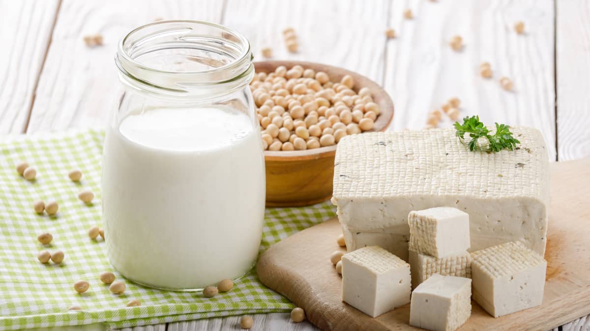 Lait de soja dans un pot et tofu sur une table en bois avec graines de soja dans un bol
