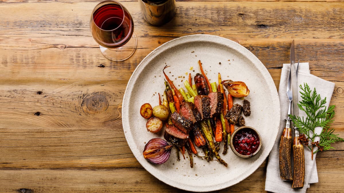 Tranches de steak de gibier grillées avec légumes cuits au four et sauce aux baies et vin rouge